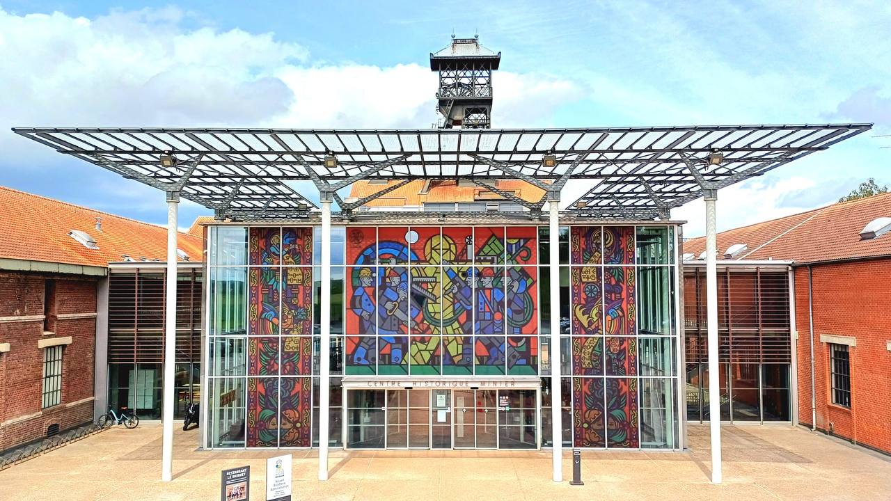 Stained-glass composition covering the full glazed entrance facade of the Centre Historique Minier, Lewarde, with the pit headframe behind