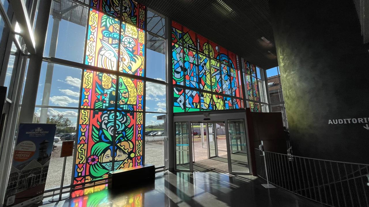 Coloured light pouring through the entrance glazing, seen from inside the museum foyer, Lewarde